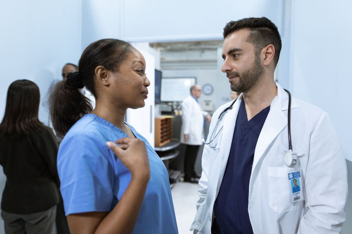 A nurse and physician talking in a bright clinic hallway